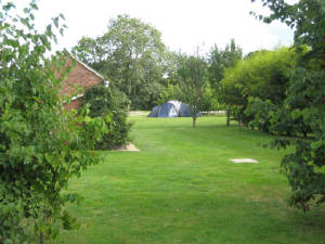 A tent pitched on the mown grass field, with the red brick building on the left