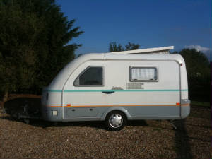 A small touring caravan on a gravel hardstanding under a deep blue sky