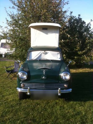 A vintage green car with a pop-up roof tent parked on a grass pitch