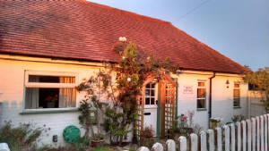 A white cottage with a red tiled roof and a picket fence in evening light