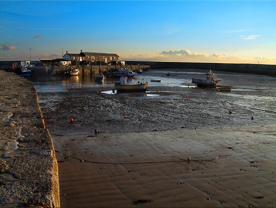 The harbour at Lyme Regis at low tide, with boats on the sand at sunset