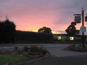 Sunset over the hedges and trees, with the site lit up below