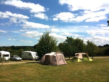 Tents and touring caravans on the grass under a big blue sky